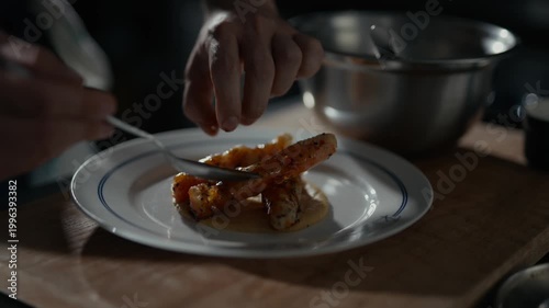Chef plates dish with care. Crispy fish rests on creamy bed. Green leaf adds vibrant contrast. Wooden board and metal bowl in background. Dinner scene, calm, focused, and precise