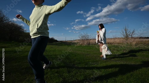 A Happy Family with Parents and Two Daughters Enjoys a Sunny Spring Day, Playing and Bonding in a Green Field Filled with Wildflowers.
