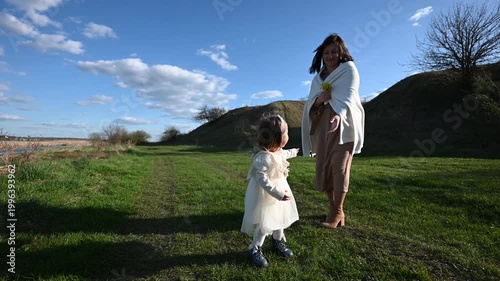 Loving Mother and Daughter Enjoy a Joyful Walk Together Through a Lush Green Field Under a Clear Blue Sky, Fostering Their Special Family Bond in Nature.