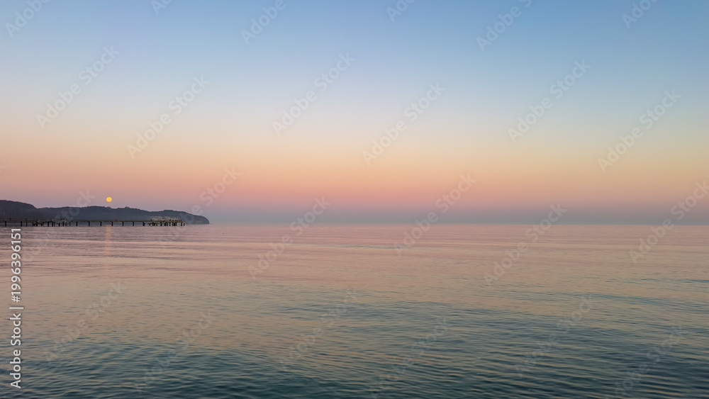 Fototapeta premium Calm sunset over the sea with a wooden pier and full moon. Peaceful twilight landscape.