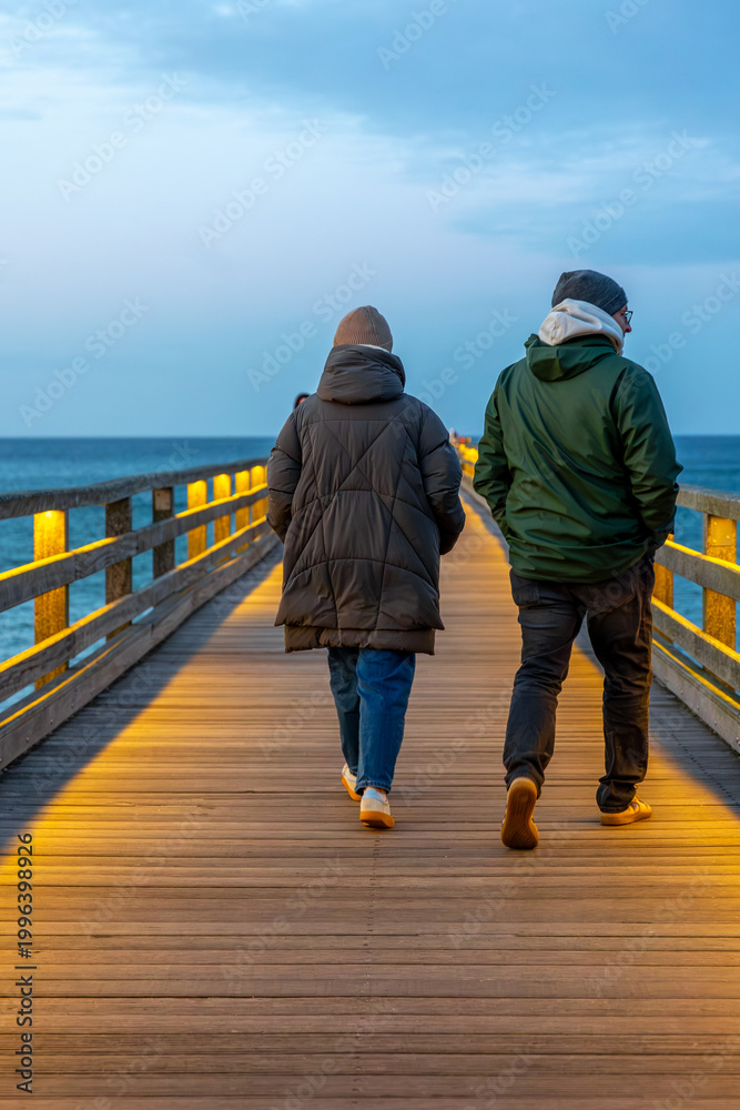 Fototapeta premium Couple walking on wooden pier. Evening stroll by the sea.
