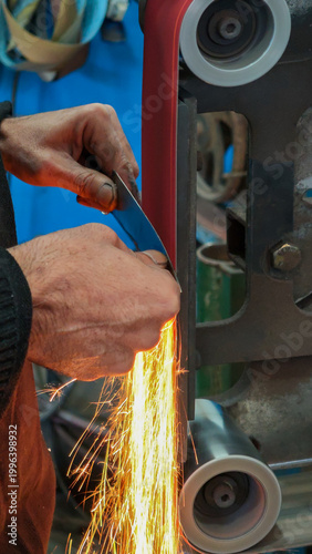 Blacksmith grinding a Damascus steel blade with sparks flying in a workshop.