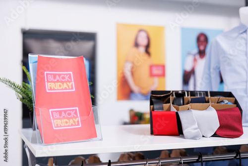 Red Black Friday flyer on cloth rack in retail store, close up of promo banner. Sale marketing and retail business concept, visual merchandising in clothing shop during seasonal sales