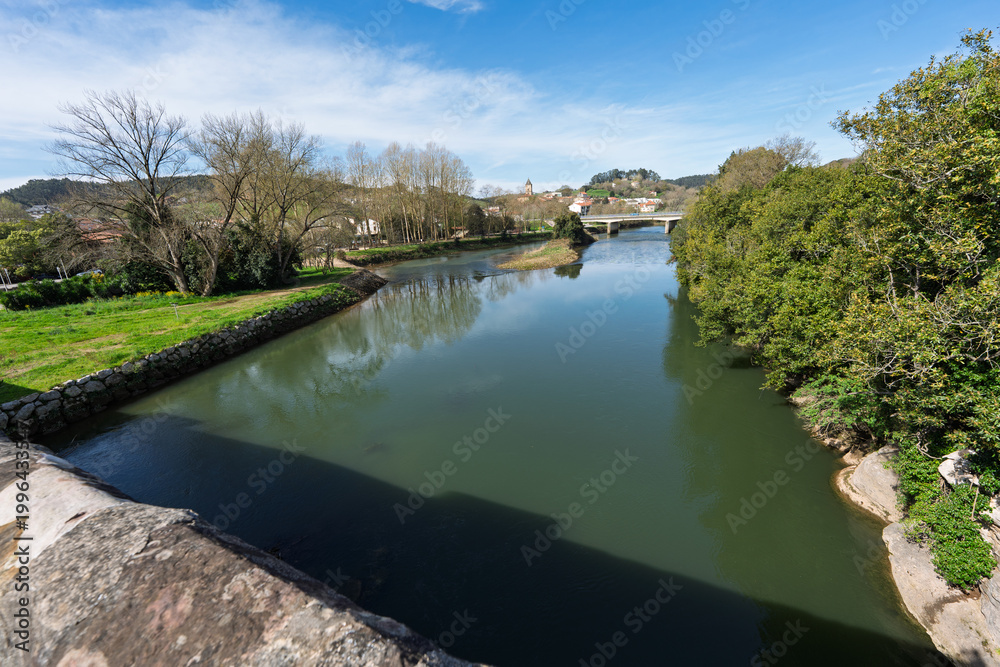 Fototapeta premium Peaceful River Landscape With Bridge and Village Under Blue Sky