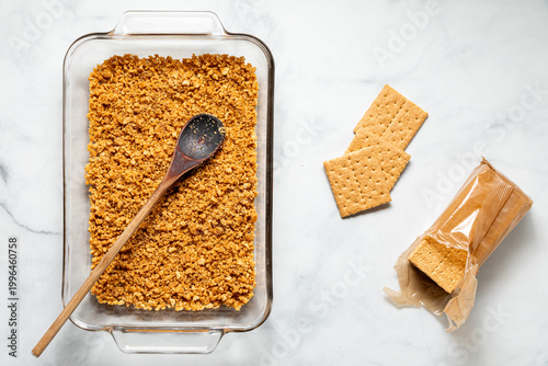 Top down view of a baking dish with a graham cracker crust prior to baking.