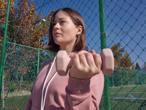 Woman doing outdoor strength training with dumbbell on sports court.