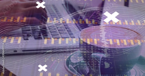 Writing hand holding pen marking spiral notebook at office, with laptop, cup, data overlays