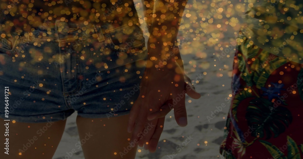 Obraz premium Holding hands couple standing on sand, wearing denim cutoff shorts, colorful garment, golden bokeh