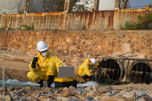 Photography Environmental engineers in yellow hazmat suits collecting water samples from industrial drainage pipes for pollution and contamination testing