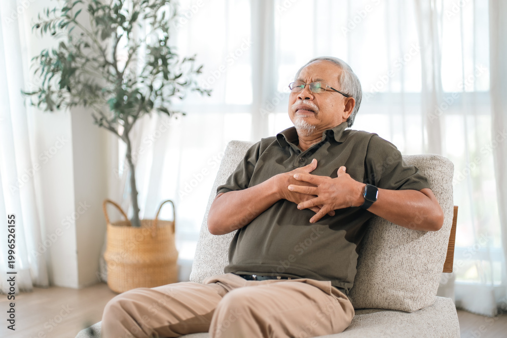 Fototapeta premium Elderly health insurance, elderly man chest pain sitting on chair at home, eyes closed and hand on chest with discomfort