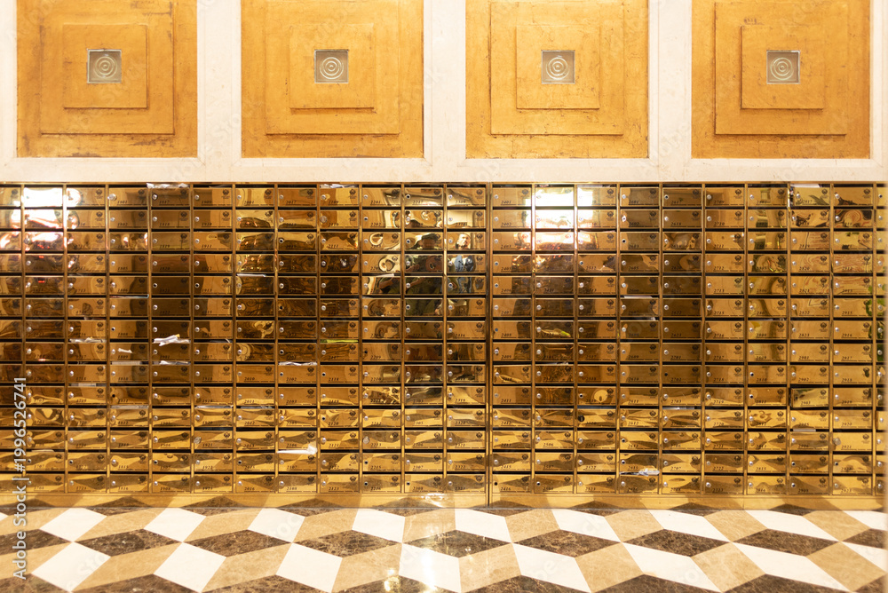 Fototapeta premium Golden mailbox wall, mirrored metal mailbox grid in lobby with geometric floor and warm light