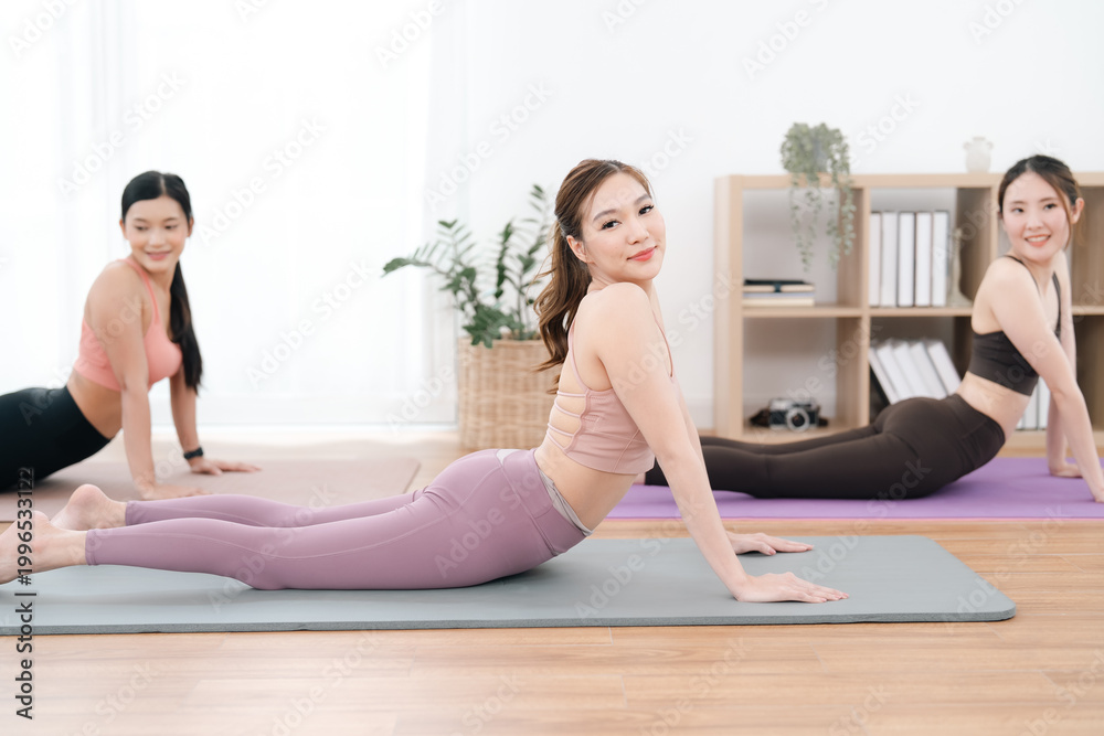 Obraz premium Exercise class in bright studio, three women doing yoga pose on mat, calm fitness practice with stretching and healthy lifestyle