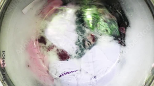 Close up of clothes being washed in a washing machine, seen through the outside glass. The washing machine shows the clothes and the foam being spun.