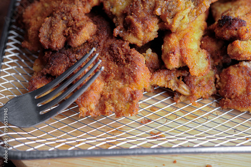 Milanesas de pollo pescado o camarones empanizados o carne de res en una rejilla de aluminio con un tenedor al lado, vista con angulo y con acercamiento o macro.