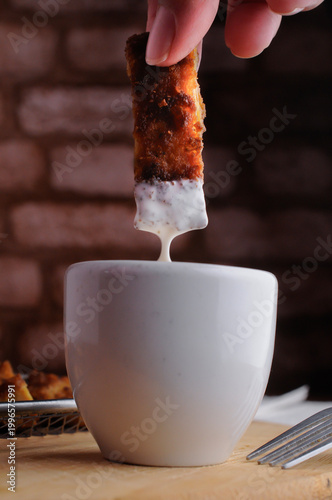 Milanesas de pollo pescado o camarones empanizados con un tazoncito de ranch o gravy para sazonar, sobre una tabla de cortar de madera