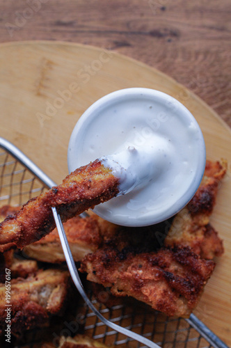 Milanesas de pollo pescado o camarones empanizados con un tazoncito de ranch o gravy para sazonar, sobre una tabla de cortar de madera