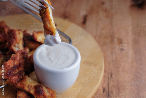 Milanesas de pollo pescado o camarones empanizados con un tazoncito de ranch o gravy para sazonar, sobre una tabla de cortar de madera