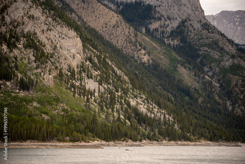 Breathtaking panoramic view of Lake Minnewanka in Banff National Park, Alberta, Canada. Large glacial lake surrounded by the majestic Canadian Rockies, evergreen pine forests, and a clear blue sky.