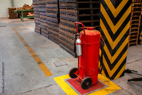 A large mobile red fire extinguisher on wheels positioned in an industrial warehouse setting with safety markings on the floor, providing emergency fire protection and workplace safety in Brazil.