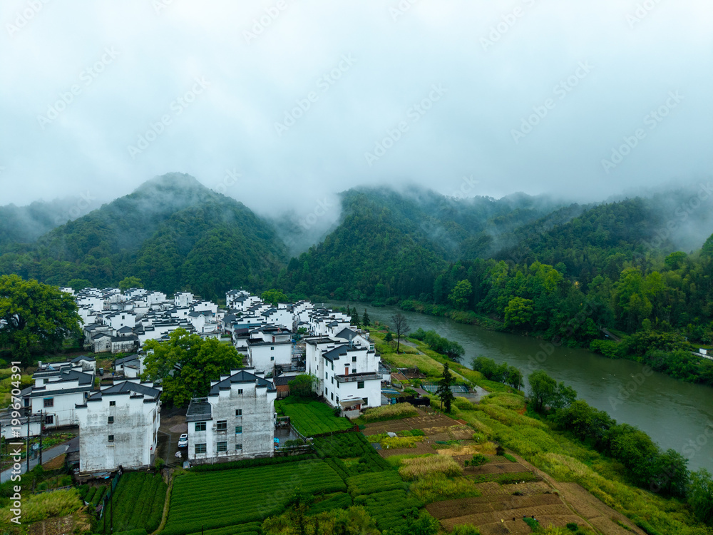 Fototapeta premium An aerial view reveals traditional white houses of Huizhou Ancient City in She County, Anhui, China, nestled by a winding river and lush misty mountains