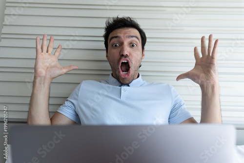 Принти на полотні Surprised man with his hand raised reacting to unexpected content on his laptop at home