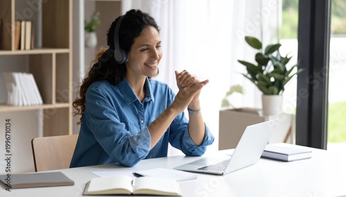 Smiling woman with headphones working on laptop at home office.