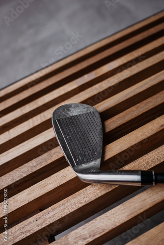 Close-up of golf iron club head on wooden slatted bench
