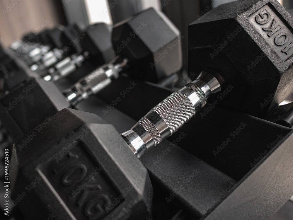 Fototapeta premium Close-up and row of black hex dumbbells on rack in modern gym