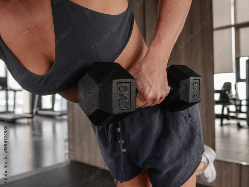 Fototapeta premium Athletic woman performing one arm dumbbell row on bench in modern gym