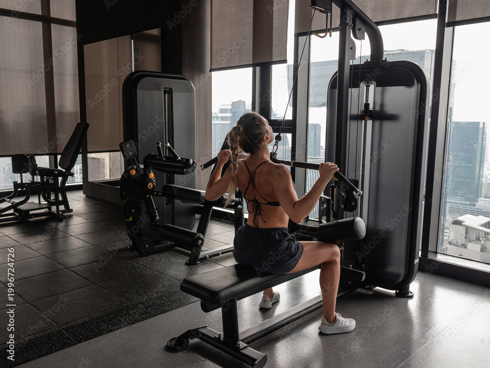 Naklejka premium Athletic woman performing lat pulldown exercise on cable machine in modern gym