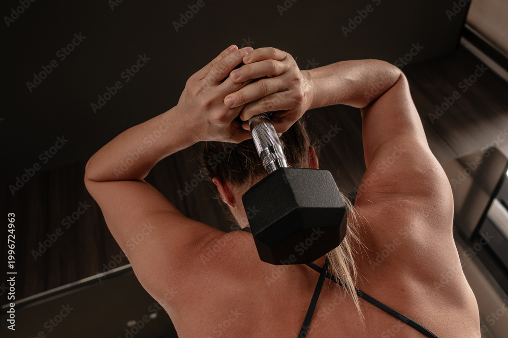 Fototapeta premium Athletic woman performing overhead dumbbell triceps extension exercise in gym