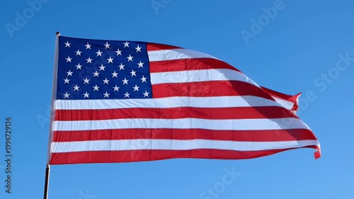 American flag waving in slow motion against a clear blue sky patriotic symbol of freedom and democracy.
