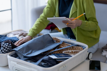 Happy asian Woman doing checklist for packing suitcase before holidays trip.