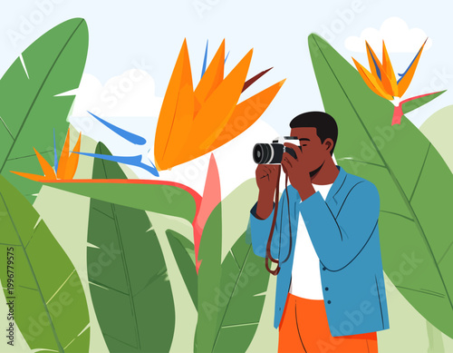 A man photographing vibrant Bird of Paradise flowers in a lush tropical garden setting.