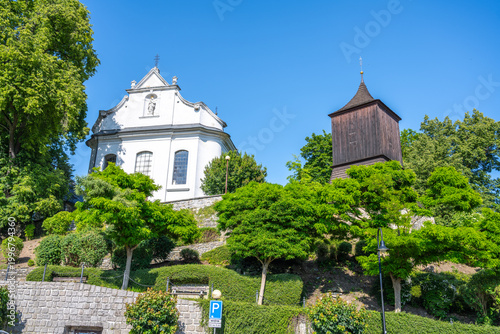 Visitors can see St. James the Greater Church in Zelezny Brod. The church stands on a hill surrounded by green trees and offers views of the town below. The weather is clear.