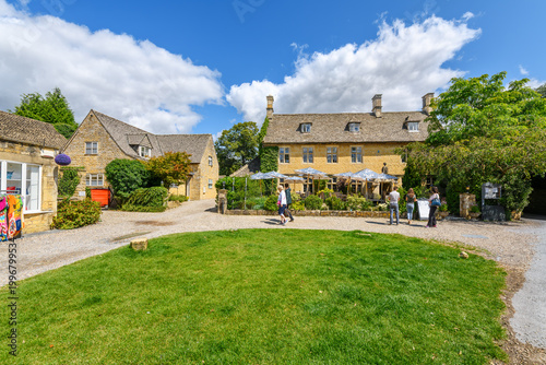 A small grassy park and public square with shops and cafes in the center of the Cotswold Village of Bourton-on-the-Water, England.