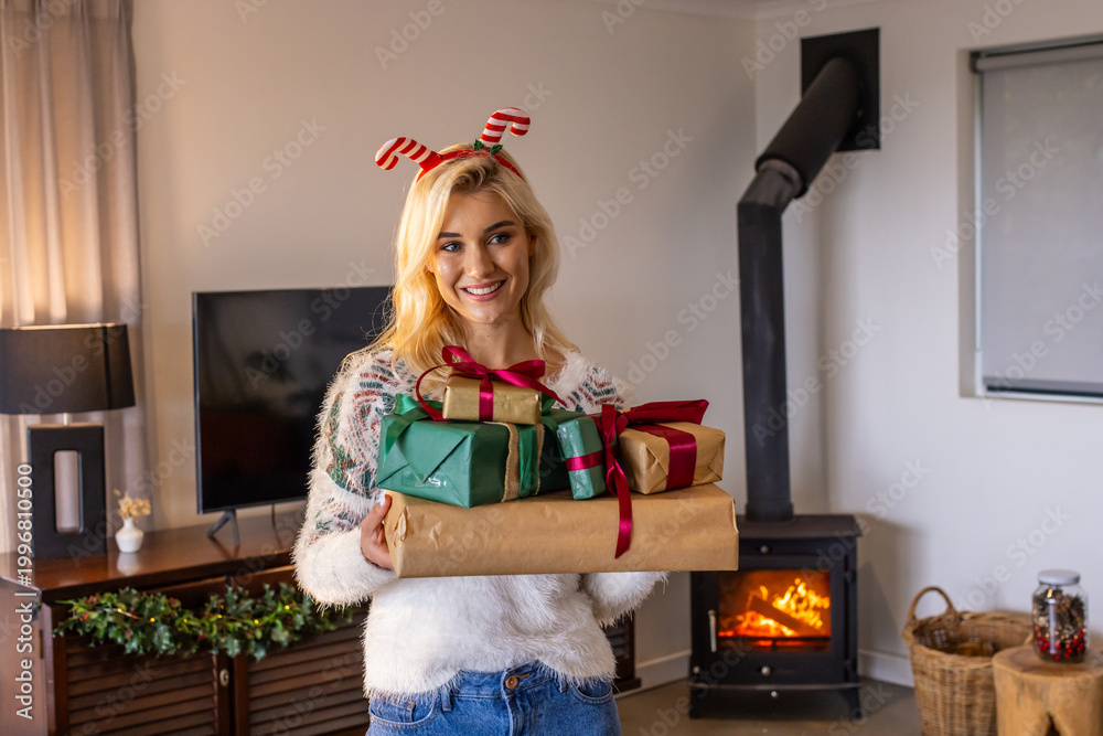 Naklejka premium Woman in twenties standing at home holding wrapped gifts wearing fuzzy sweater festive headband