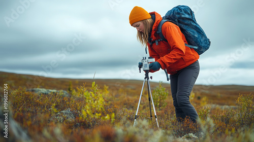 A female scientist in a bright orange jacket sets up equipment in a remote field for research purposes