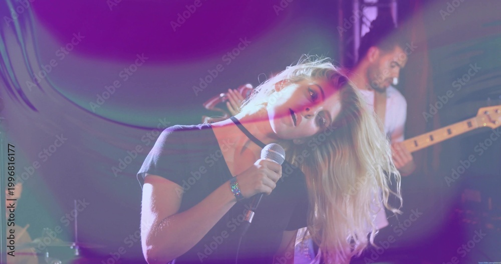 Fototapeta premium Singing lead singer leaning head to side on club stage, holding wired mic, wearing choker