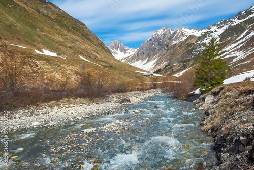 beautiful landscape in French Alps in Tarentaise valley with rocky peak mountains in background  with  some snow and clear water from a stream flowing in valley