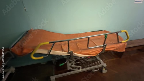 Medical gurney with orange mattress in a hospital corridor with peeling paint on wall