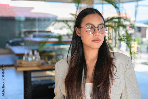 A serious Asian woman from Thai Isan looking away while wearing glasses in a professional cafe.