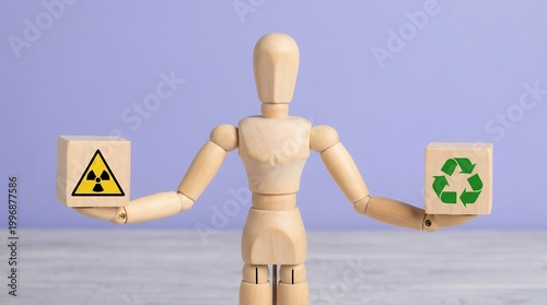 A wooden artist mannequin holds cubes displaying radioactivity and recycling symbols symbolizing environmental choices and energy dilemmas hazard danger safety sustainable