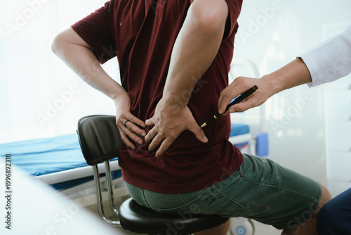 Fotografía Doctor explaining spine anatomy with a model to a male patient experiencing lower back pain in a clinic, discussing diagnosis and treatment options