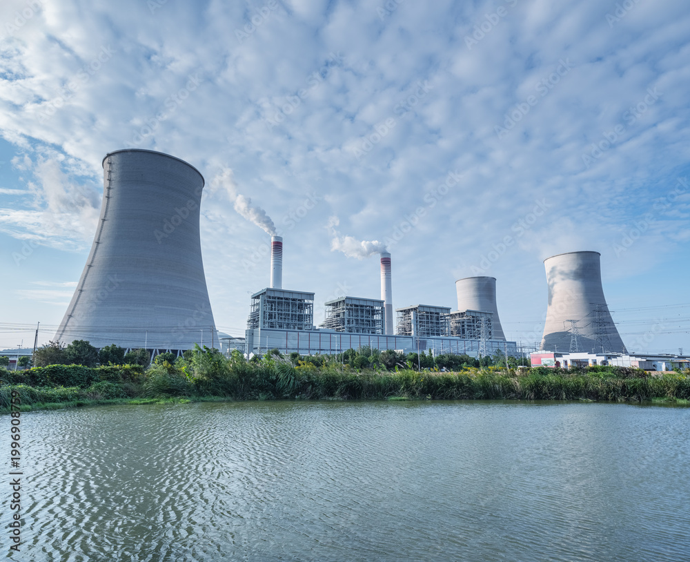 Fototapeta premium Large-Scale Coal-Fired Power Plant with Cooling Towers Near Pond Under Cloudy Sky