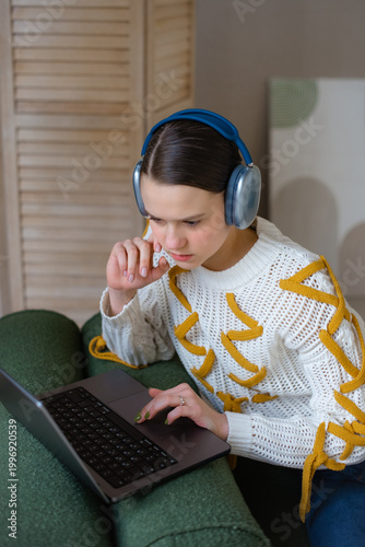 teenage girl with laptop in wireless headphones studying online at home