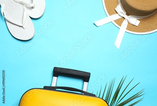 Foto Composition with suitcase, flip-flops and sunhat on bright blue background