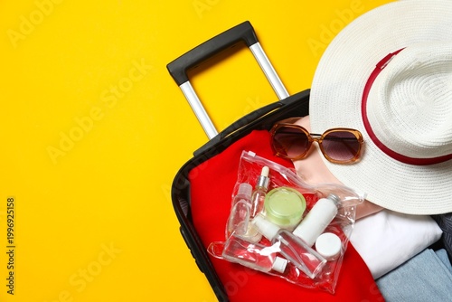 Open suitcase with clothes and travel accessories on yellow background. Various color patterns