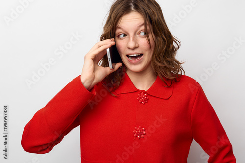 Cuadro en lienzo Young woman in red sweater talks on smartphone with surprised expression