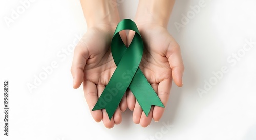 Hands holding green awareness ribbon on white surface for health campaign support